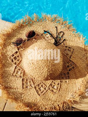 Occhiali da sole e cappello di paglia sul lato della piscina in marmo con acqua blu chiara Foto Stock