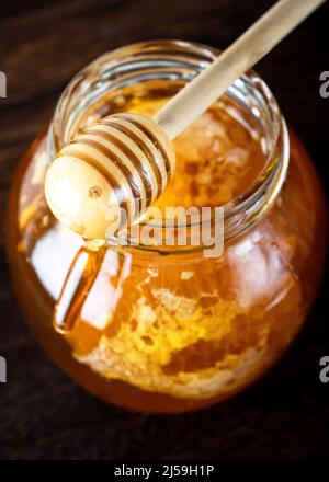 Cucchiaia di miele che versa il miele nel vaso. Cucchiaia di miele di legno che prende il miele dal vaso. Foto Stock