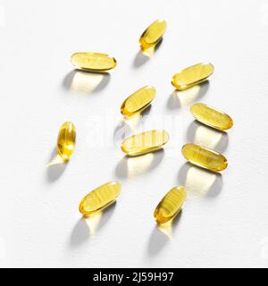 La luce del sole passa attraverso alcune capsule di Omega-3 adagiate su uno sfondo bianco. Luce caustica. Softgel di olio di pesce. Supporto medico e trattamento. Foto Stock