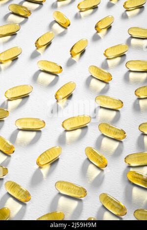 La luce del sole passa attraverso le capsule di Omega-3 adagiate su uno sfondo bianco. Luce caustica. Softgel di olio di pesce. Supporto medico e trattamento Foto Stock