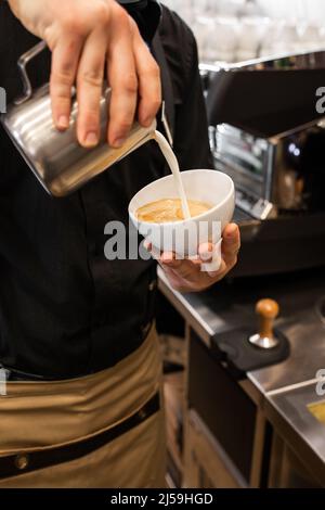 Il barista professionale versa il latte cotto a vapore in una tazza di vetro del caffè, creando un bellissimo motivo Rosetta di latte art in un bar. Caffè appena macinato. Bere Foto Stock