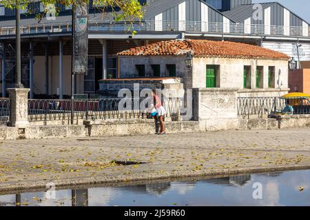 Una giovane donna cubana è vista con un bambino in un'architettura coloniale a Old Havana. Ci sono acque stagnanti in strada. L'edificio coloniale continua Foto Stock