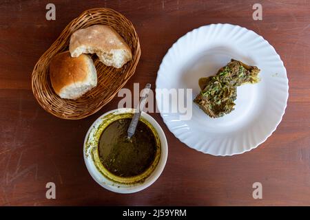 Vista dall'alto dell'autentico piatto di Goan Chicken Cafreal e pane di Goan consumato a metà Foto Stock