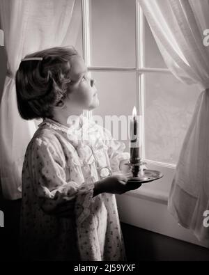 1950S BAMBINA CHE INDOSSA PIGIAMI IN PIEDI GUARDANDO FUORI DA UNA FINESTRA CHE TIENE UNA CANDELA ILLUMINATA - J5943 HAR001 SODDISFAZIONE HARS FEMMINE STUDIO SHOT HOME VITA COPIA SPAZIO HALF-LENGTH ISPIRAZIONE CARING PIGIAMA SIMBOLI SPIRITUALITÀ DESIDERIO B&W PROTEZIONE ALLEGRO ILLUMINATO SPERANZA ANTICIPAZIONE BUONE NOTIZIE DICEMBRE CONCETTO CONCETTUALE DICEMBRE 25 BEACON IMMAGINAZIONE DESIDERIO SIMBOLICO CONCETTI CRESCITA GIOIOSA GIOVANI NERO E BIANCO ETNIA CAUCASICA HAR001 RAPPRESENTAZIONE IN VECCHIO STILE Foto Stock