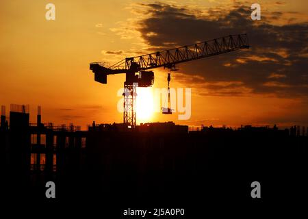 Silhouette nera della gru a torre con carico e lavoratori su ponteggio all'alba. Edilizia abitativa, condominio in città Foto Stock