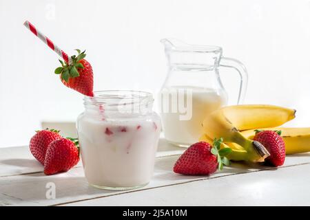 Yogurt alla fragola e alla banana in vaso con paglia e fragola su legno bianco con fragole e banane Foto Stock