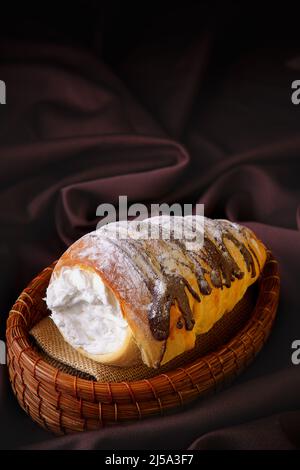 delizioso pane a forma di cono arrotolato ripieno di crema di pasticceria ricoperta di cioccolato fatto in casa e zucchero posto su un recipiente rustico Foto Stock