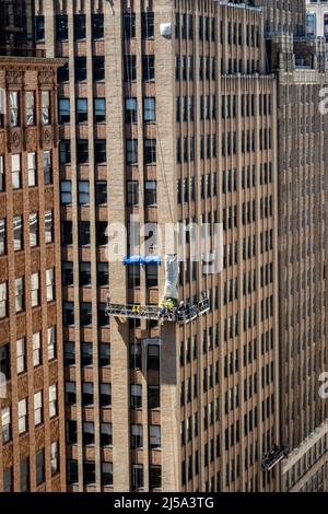 Team di lavoratori che sostituiscono mattoni su un ufficio edificio facciata mentre si lavora in un carro sospeso 15 Stories Up , NYC, USA, 2022 Foto Stock