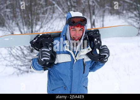 Ritratto di uno snowboarder su una pista innevata. Freerider con uno snowboard in un cappello e una maschera di montagna Foto Stock