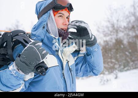 Ritratto di uno snowboarder su una pista innevata. Freerider con uno snowboard in un cappello e una maschera di montagna Foto Stock
