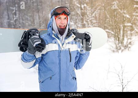 Ritratto di uno snowboarder su una pista innevata. Freerider con uno snowboard in un cappello e una maschera di montagna Foto Stock