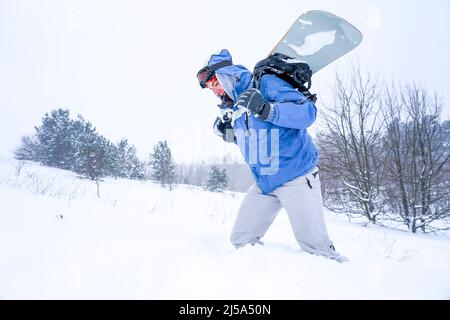 Il ragazzo snowboarder va su una pista innevata. Ha in mano uno snowboard Foto Stock