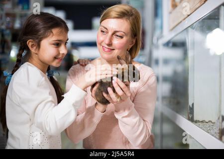 Madre con la sua figlia che tiene insieme coniglio al deposito dell'animale domestico Foto Stock