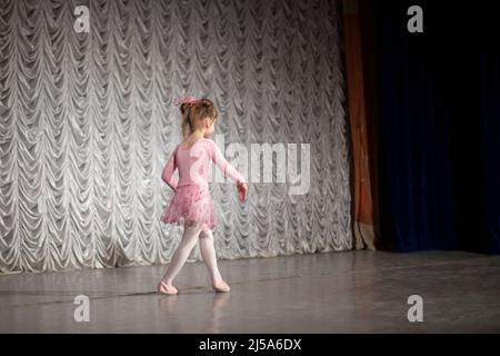 Una ragazza in un vestito rosa sta ballando sul palco. Un bambino di una scuola di danza. La ragazza mostra movimenti di danza. Foto Stock