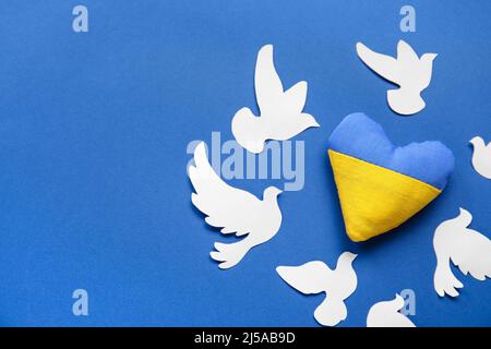 Cuore nei colori della bandiera Ucraina e colombe di carta come simbolo di pace su sfondo blu Foto Stock