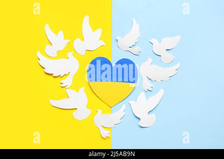 Cuore nei colori della bandiera Ucraina e colombe di carta come simbolo di pace su sfondo giallo e blu Foto Stock