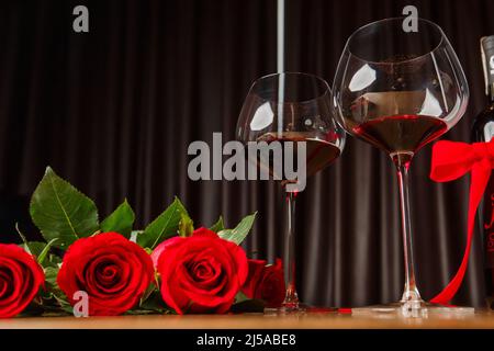 Cena romantica. Bouquet di fiori adagiato sul tavolo, fuoco selettivo su mazzo di rose, due bicchieri di vino rosso sul tavolo di legno. Data concetto, b Foto Stock