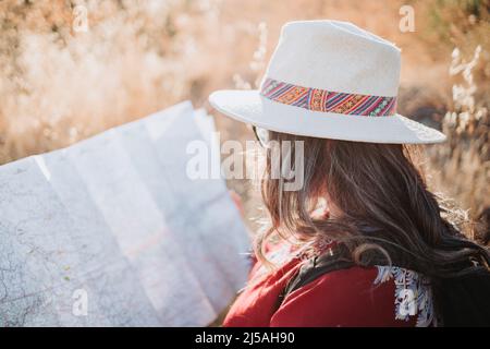 Primo piano di una donna viaggiatore che indossa un cappello, un poncho rosso e uno zaino, controllando la mappa durante il trekking per esplorare la natura Foto Stock