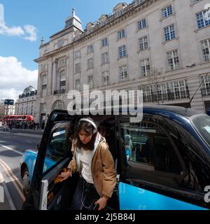 Londra, Greater London, Inghilterra, aprile 09 2022: Cliente con cuffie che esce da un taxi aka taxi su Regent Street con un autobus in background. Foto Stock