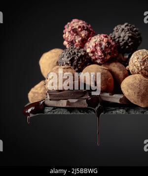 Deliziosi tartufi di cioccolato e gocce di salsa di cioccolato su sfondo nero. Foto Stock