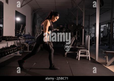 Fitness donna facendo affondo esercizi con manubri nelle sue mani per addestrare i muscoli delle gambe in palestra. Ragazza attiva squats su una gamba. Foto Stock