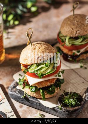 Due deliziosi hamburger fatti in casa di manzo, formaggio, verdure e microgreens su un vecchio asse di legno su sfondo verde. Composizione per esterni Foto Stock