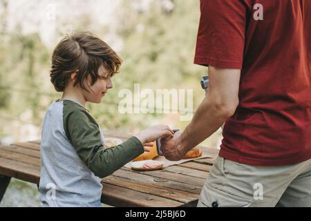 Vista ravvicinata del padre e del figlio del ragazzo della scuola in un picnic in famiglia in montagna. Bambino e suo padre che si riposa e si gode un pic-nic mentre Foto Stock