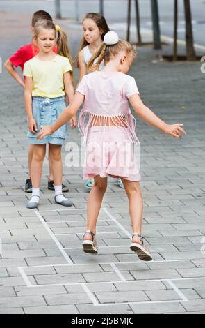 Bambini in età scolastica elementare che giocano hopscotch Foto Stock