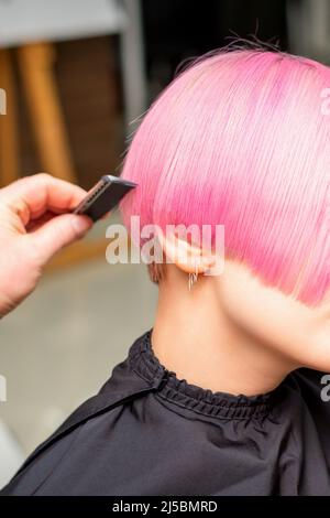 Un parrucchiere sta pettinando i capelli corti rosa tinti del cliente femminile in un salone del parrucchiere Foto Stock