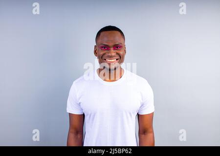 afro american uomo in bianco t-shirt casual stile con eyeshadow rosa e rossetto crossdressing in moda show studio sfondo Foto Stock