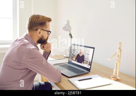 Uomo serio che guarda una videoconferenza o che ha un corso online con un insegnante remoto sul laptop Foto Stock