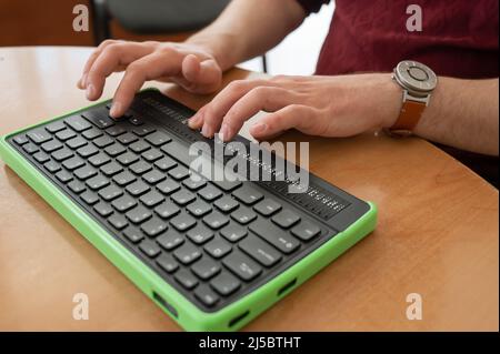 Un uomo cieco utilizza un computer con un display Braille e una tastiera per computer. Dispositivo incluso. Foto Stock