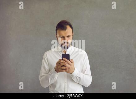 Uomo d'affari caucasico calmo e calmo con smartphone, in piedi su sfondo grigio. Foto Stock