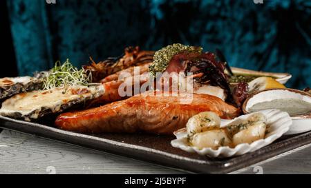 Pesce misto arrosto con cozze, gamberi, salmone, calamari e aglio di pesce Barracuda alla griglia con salsa piccante al peperoncino. Frutti di mare e carne plat Foto Stock