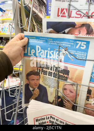 Parigi, Francia - Apr 21, 2022: POV maschio mano buy le Parisien giornale stampa titoli dopo dibattito tra Marine le Pen e il presidente francese Emmanuel Macron - elezione presidenziale del 2022 Foto Stock