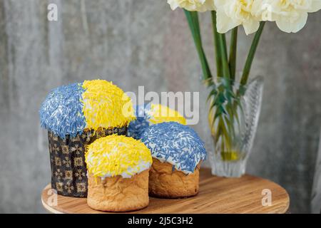 Dolci di Pasqua deliziosi nei colori della bandiera Ucraina, giallo e blu su un tavolo di legno con fiori sullo sfondo. Luogo per il testo. selecti Foto Stock