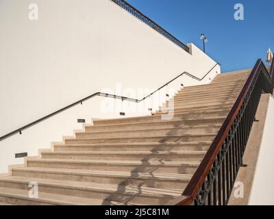 Ampia scala verso il cielo con scalini in pietra lungo una parete luminosa. Concetto di crescita professionale. Foto Stock