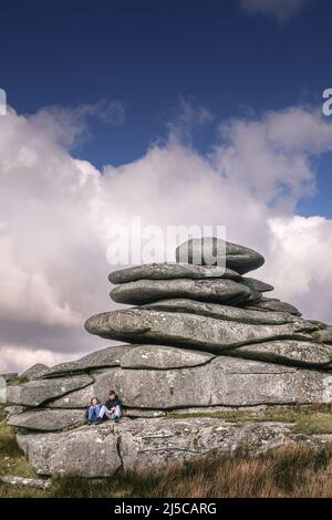 Una giovane coppia che si rilassa sotto un torreggiante scoglio di granito lasciato dall'azione glaciale su Stowes Hill a Bodmin Moor in Cornovaglia. Foto Stock