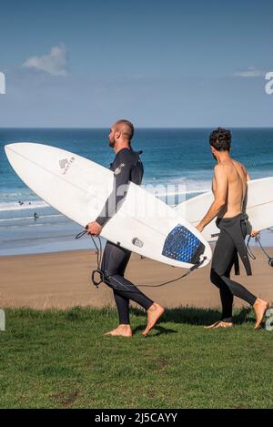 Due surfisti maschi che trasportano le loro tavole da surf e camminano sulla costa fino al mare a Newquay in Cornovaglia. Foto Stock