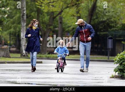 Finalmente uscire - la famiglia indossa maschere facciali in un parco pubblico mentre si pratica in bicicletta con la loro figlia giovane. [traduzione automatizzata] Foto Stock