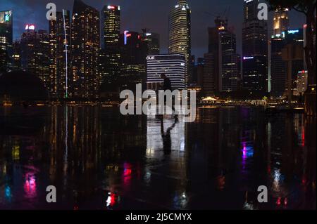 28 maggio 2020, Singapore, Repubblica di Singapore, Asia - Un pedone si distingue in silhouette contro lo skyline illuminato dei grattacieli del distretto commerciale a Marina Bay durante il coprifuoco nella crisi di Corona (Covid-19), ed è riflesso in pozzanghere lungo il lungomare durante una tempesta di pioggia. [traduzione automatizzata] Foto Stock