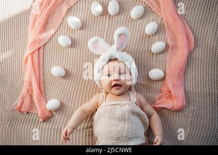 il neonato giace su un letto dai colori pastello come un coniglietto pasquale sull'erba con le uova Foto Stock