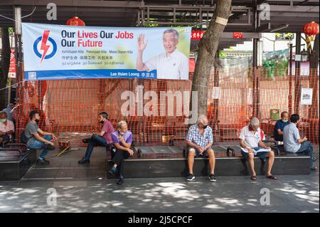 07/06/2020, Singapore, Repubblica di Singapore, Asia - gli uomini siedono sotto una bandiera di elezione del partito d'azione popolare (PAP) il primo ministro Lee Hsien Loong posto fra due alberi a Crete Ayer Square nel quartiere cinese della città. Le elezioni generali del 2020 sono previste per venerdì 10 luglio, in cui il partito PAP al potere mira a conquistare nuovi mandati in mezzo alla pandemia di Corona (Covid-19). [traduzione automatizzata] Foto Stock