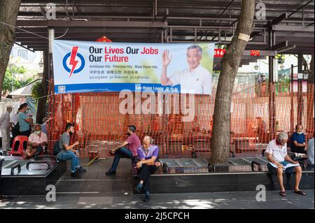 07/06/2020, Singapore, Repubblica di Singapore, Asia - gli uomini siedono sotto una bandiera di elezione del partito d'azione popolare (PAP) il primo ministro Lee Hsien Loong posto fra due alberi a Crete Ayer Square nel quartiere cinese della città. Le elezioni generali del 2020 sono previste per venerdì 10 luglio, in cui il partito PAP al potere mira a conquistare nuovi mandati in mezzo alla pandemia di Corona (Covid-19). [traduzione automatizzata] Foto Stock