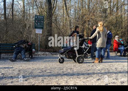 20.03.2015, Monaco, Baviera, Germania, Europa - i genitori insieme ai loro figli visitano un parco giochi pubblico nella Torre Cinese nel Giardino Inglese in una soleggiata giornata di primavera, mentre accanto ad esso un alcolico senzatetto dorme il suo ubriachezza su una panchina del parco. [traduzione automatizzata] Foto Stock