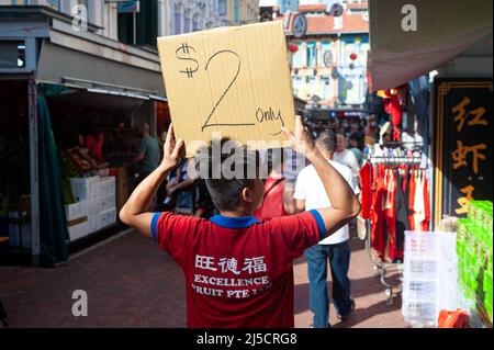 24 gennaio 2020, Singapore, Repubblica di Singapore, Asia - Un fornitore tiene un cartello di cartone con un'offerta di risparmio all'inizio della crisi di Corona mentre la gente cammina attraverso un bazar di strada trafficato nel quartiere di Chinatown della città, che si tiene ogni anno per il Capodanno cinese. Questo avviene poco dopo che la città-stato ha confermato la sua prima infezione con il coronavirus (Covid-19). [traduzione automatizzata] Foto Stock