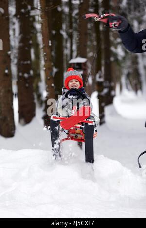 felice ragazzo in discesa su una slitta d'inverno: un bambino in abiti luminosi si siede su una slitta, la neve gli sta volando contro. Foto Stock