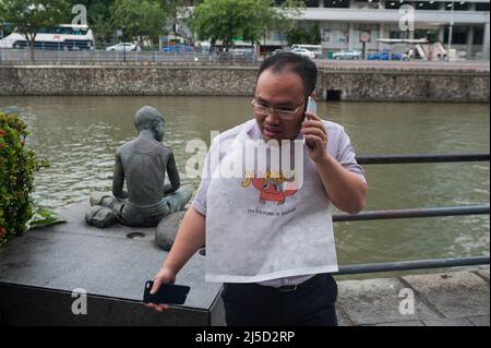 22 febbraio 2017, Singapore, Repubblica di Singapore, Asia - un uomo che indossa un lotardo da un ristorante di pesce e granchio si trova sulla riva del fiume Singapore parlando sul suo cellulare. [traduzione automatizzata] Foto Stock