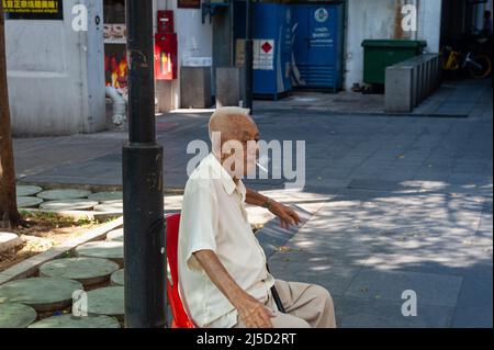 04.04.2018, Singapore, Repubblica di Singapore, Asia - un vecchio uomo siede su una sedia a Chinatown e fuma una sigaretta con piacere. [traduzione automatizzata] Foto Stock