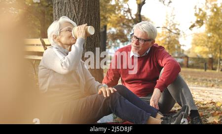 Tempo di picnic. Anziana coppia caucasica seduta su coperta al parco bere caffè, parlare, condividere ricordi preziosi. Foto di alta qualità Foto Stock
